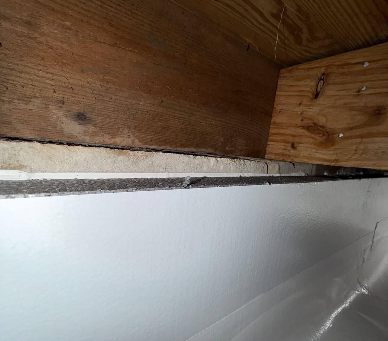 Close view of white wall liner sealed along the top edge beneath a wooden rim joist.