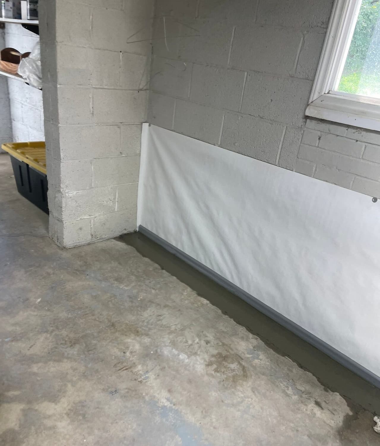 White wall liner below a basement window with a fresh concrete strip along the floor edge.