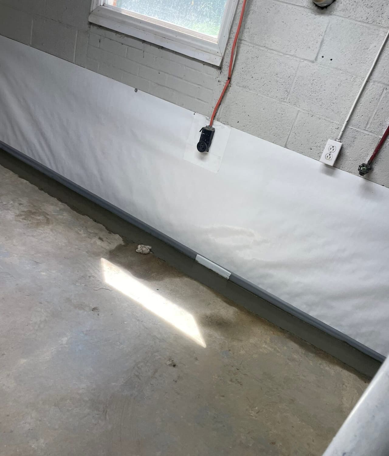 White wall liner with an outlet and cord passing through, above a concrete patched floor edge.