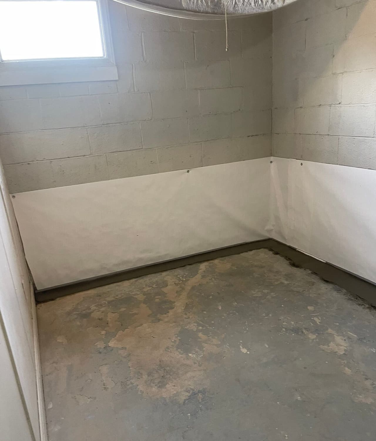 Small basement room with white liner on lower walls and concrete patched along the floor perimeter.