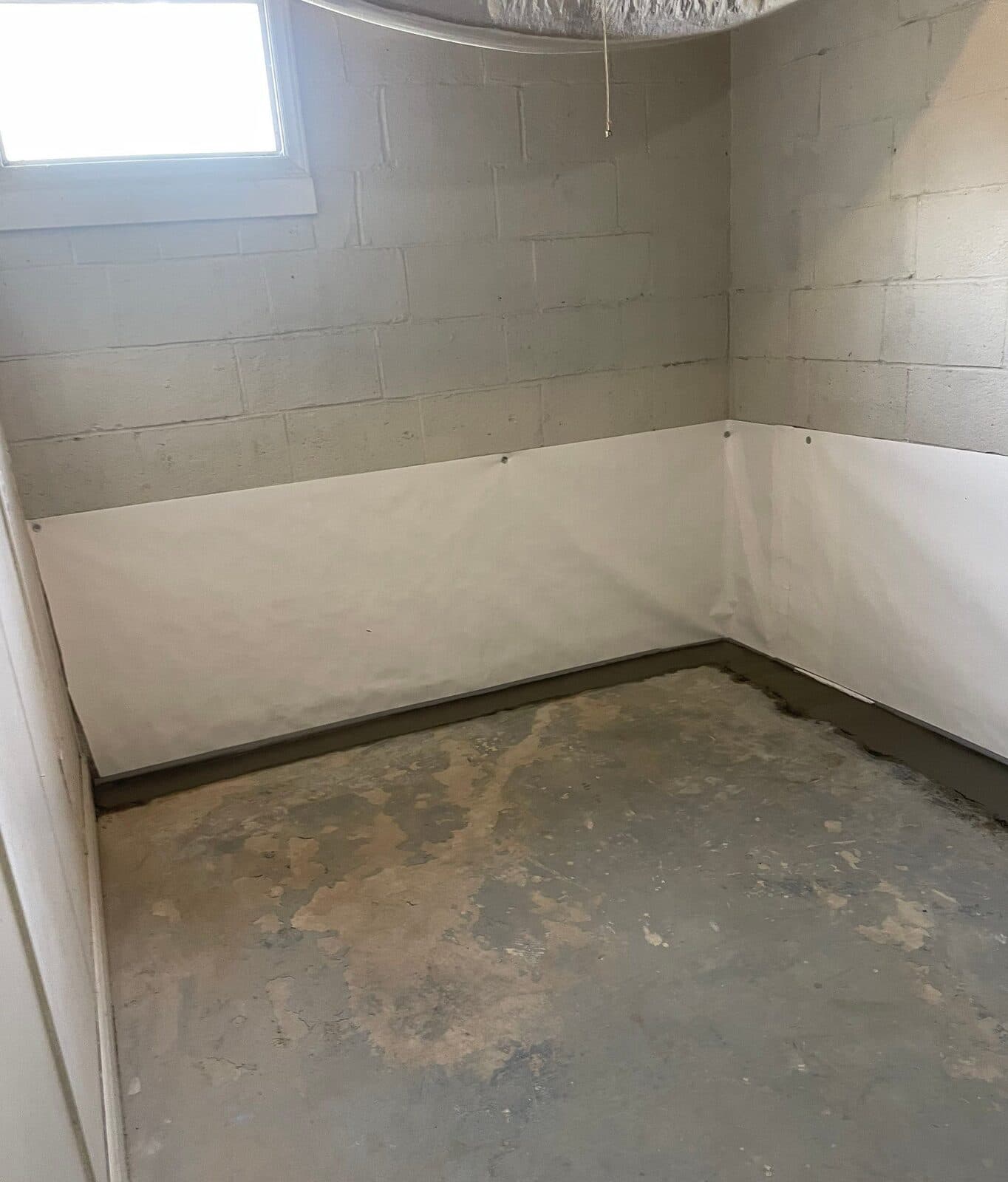 Small basement room with white liner on lower walls and concrete patched along the floor perimeter.
