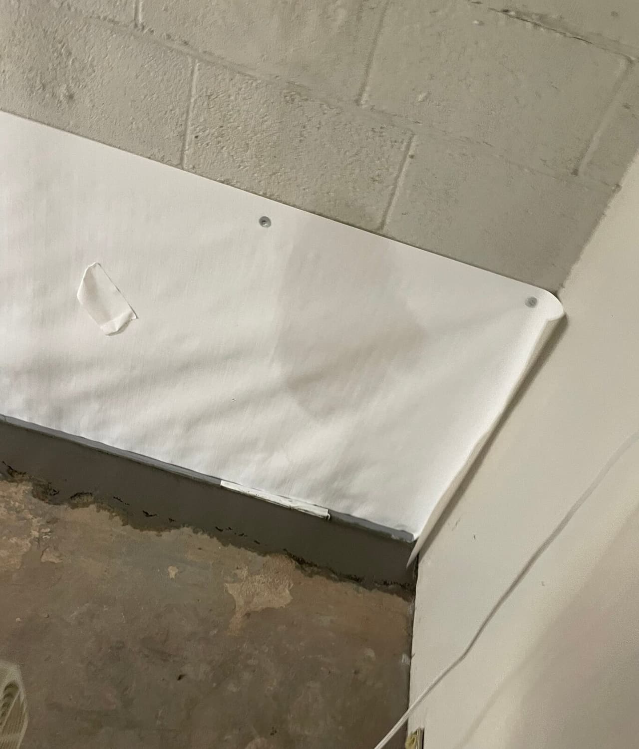 Close view of white wall liner fastened to block wall above a concrete patched floor edge.