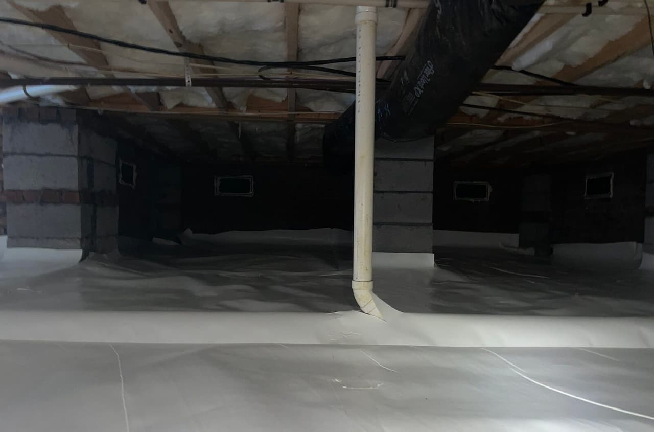 Crawl space with white liner covering the floor and wrapping block piers, with a pipe running to the floor.