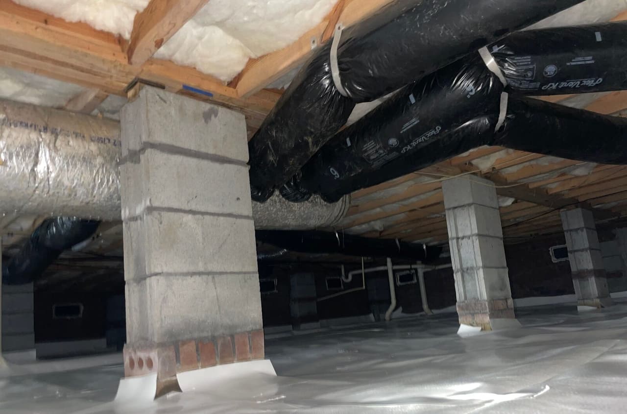 Crawl space with block piers wrapped in white liner at the base and ductwork overhead.