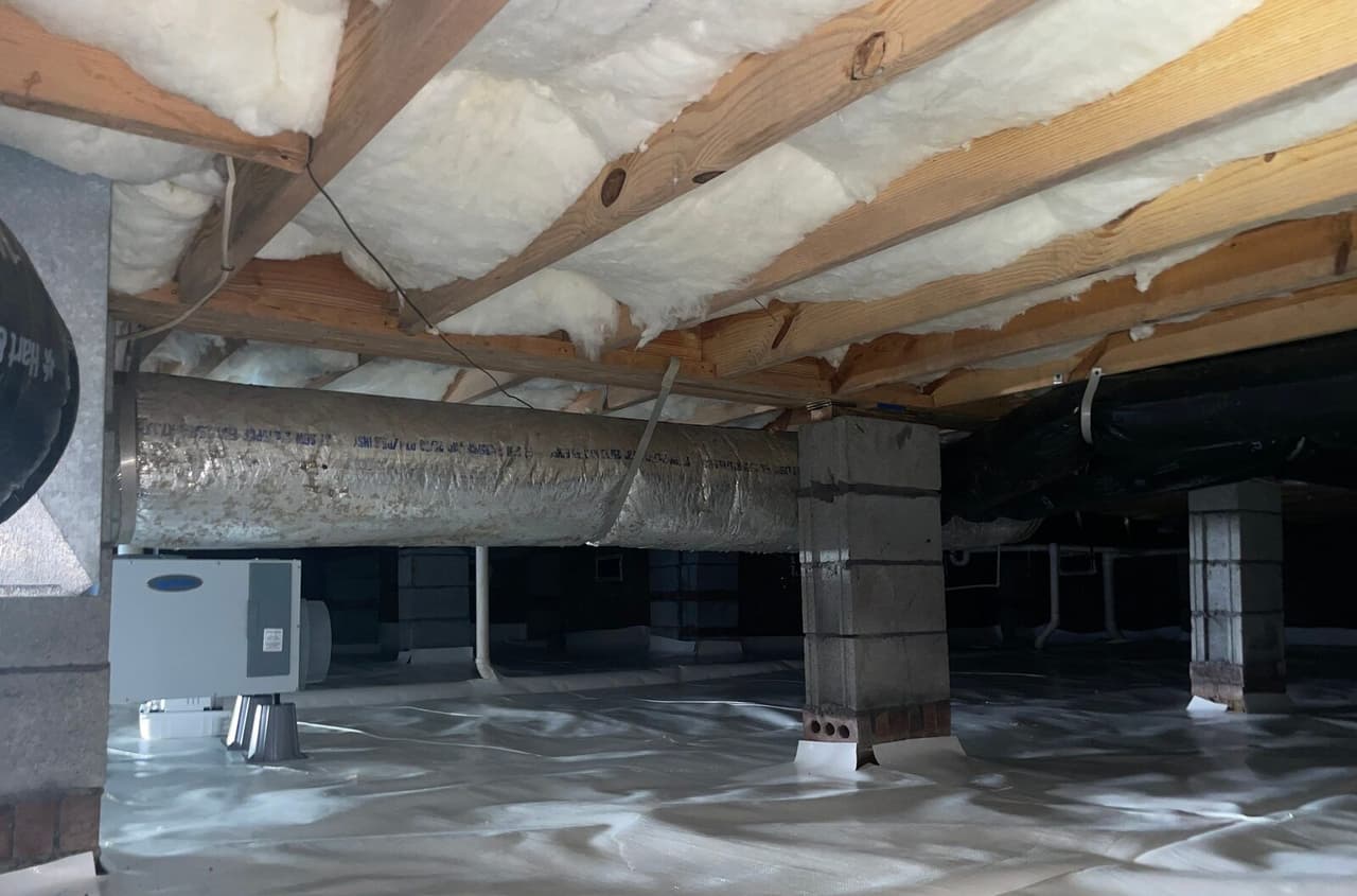 Dehumidifier set on a white lined crawl space floor near block piers and ductwork.