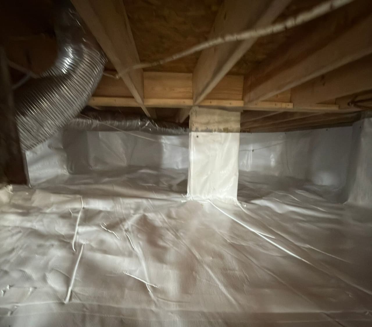 Crawl space with white liner covering the floor, foundation walls and a wrapped support pier.