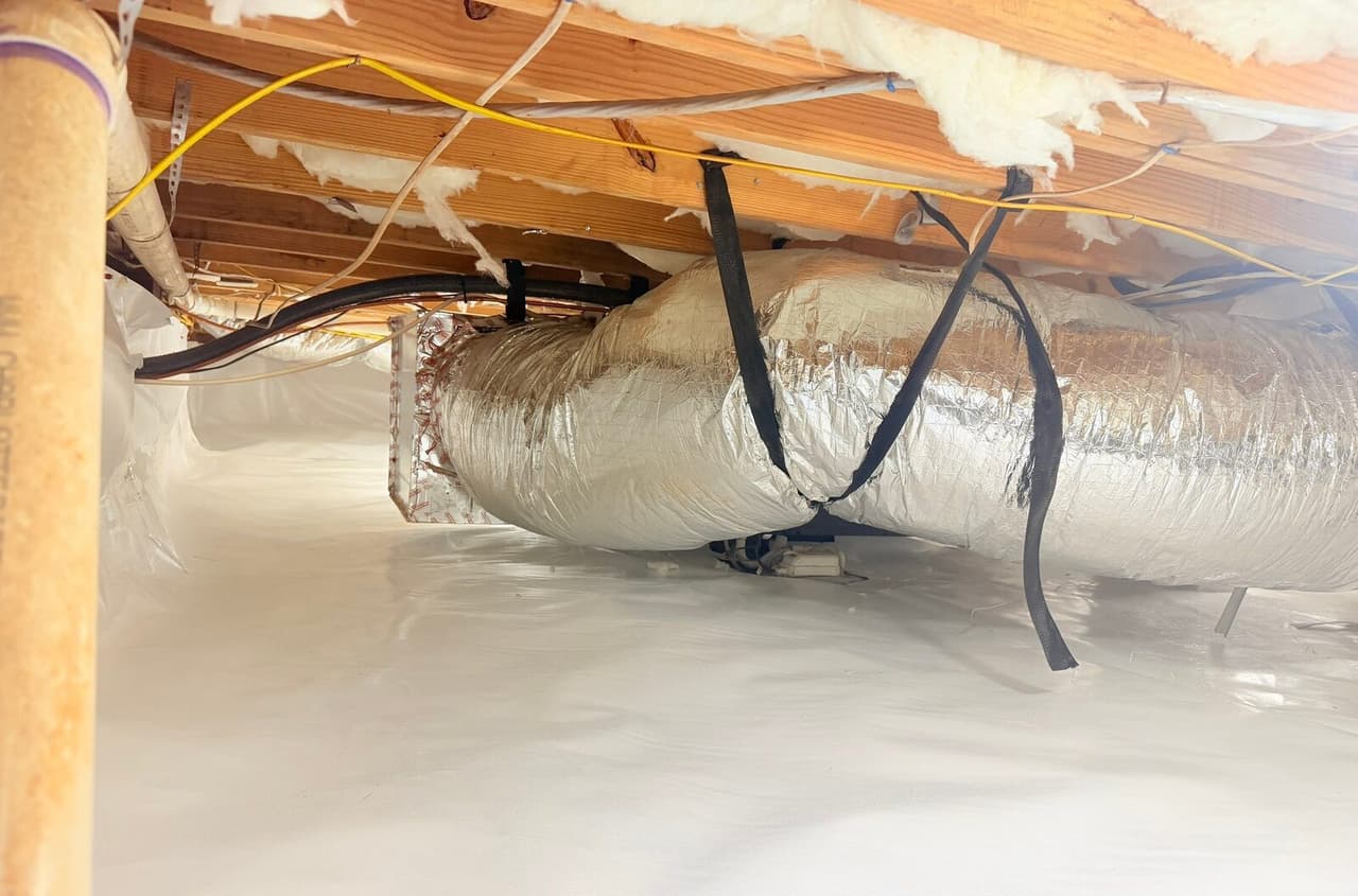 White liner covering a crawl space floor and walls beneath a foil wrapped duct and wiring.
