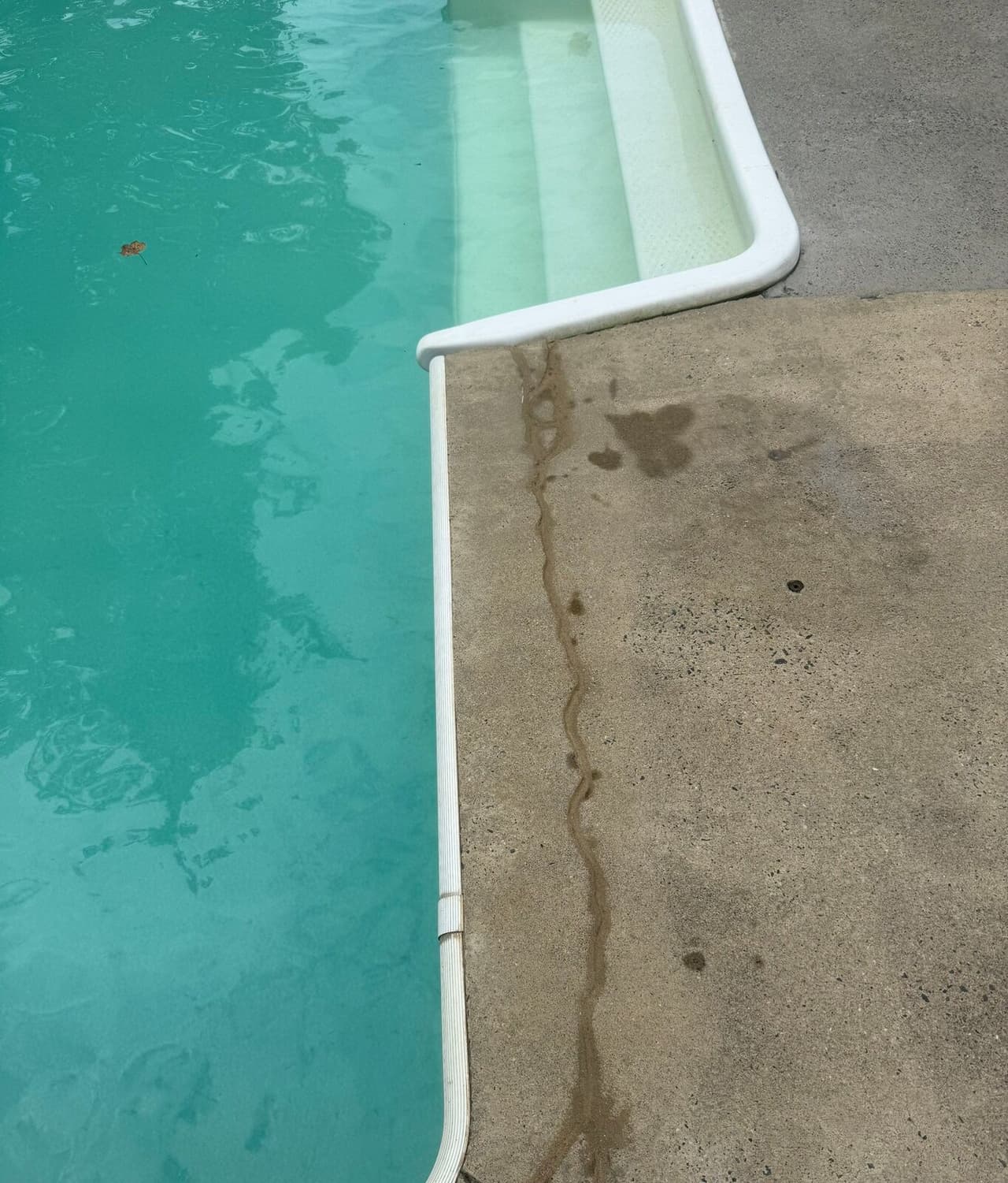 Pool deck corner beside pool steps with a sealed crack and a patched injection hole.