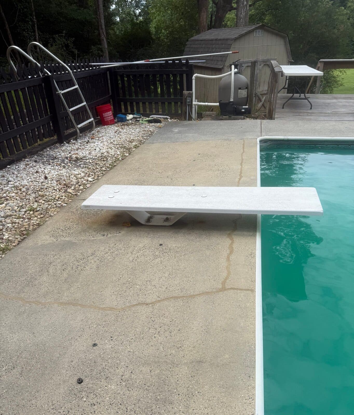 Pool deck near a diving board and pump with sealed cracks and patched injection holes.