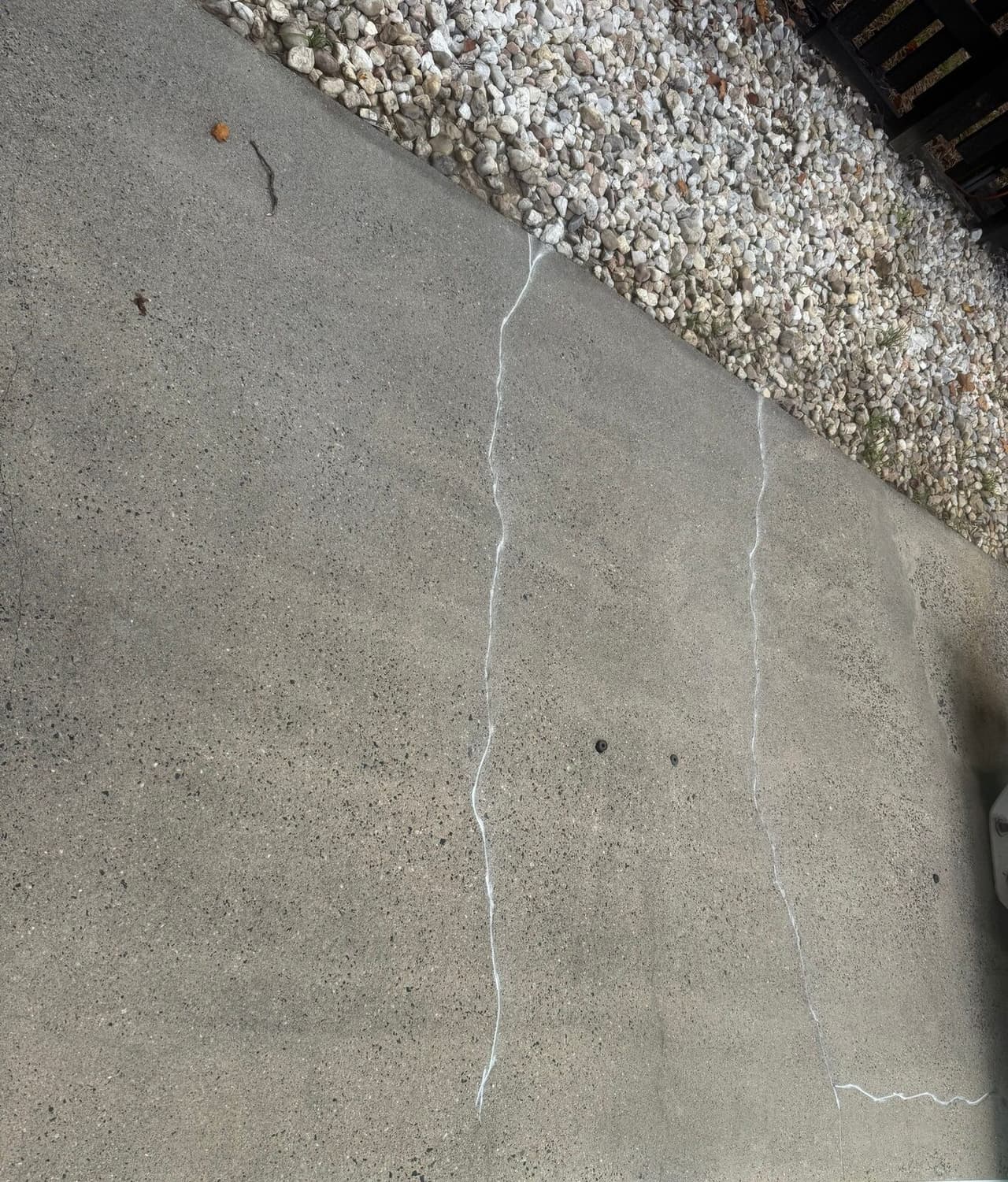 Concrete slab beside gravel with white sealant in cracks and patched injection holes.