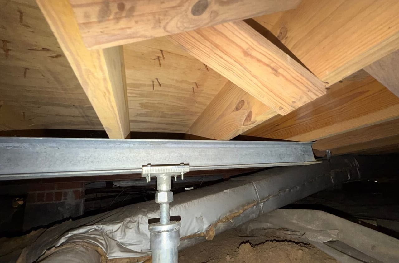 Steel beam under floor joists supported by an adjustable steel post next to insulated ductwork.