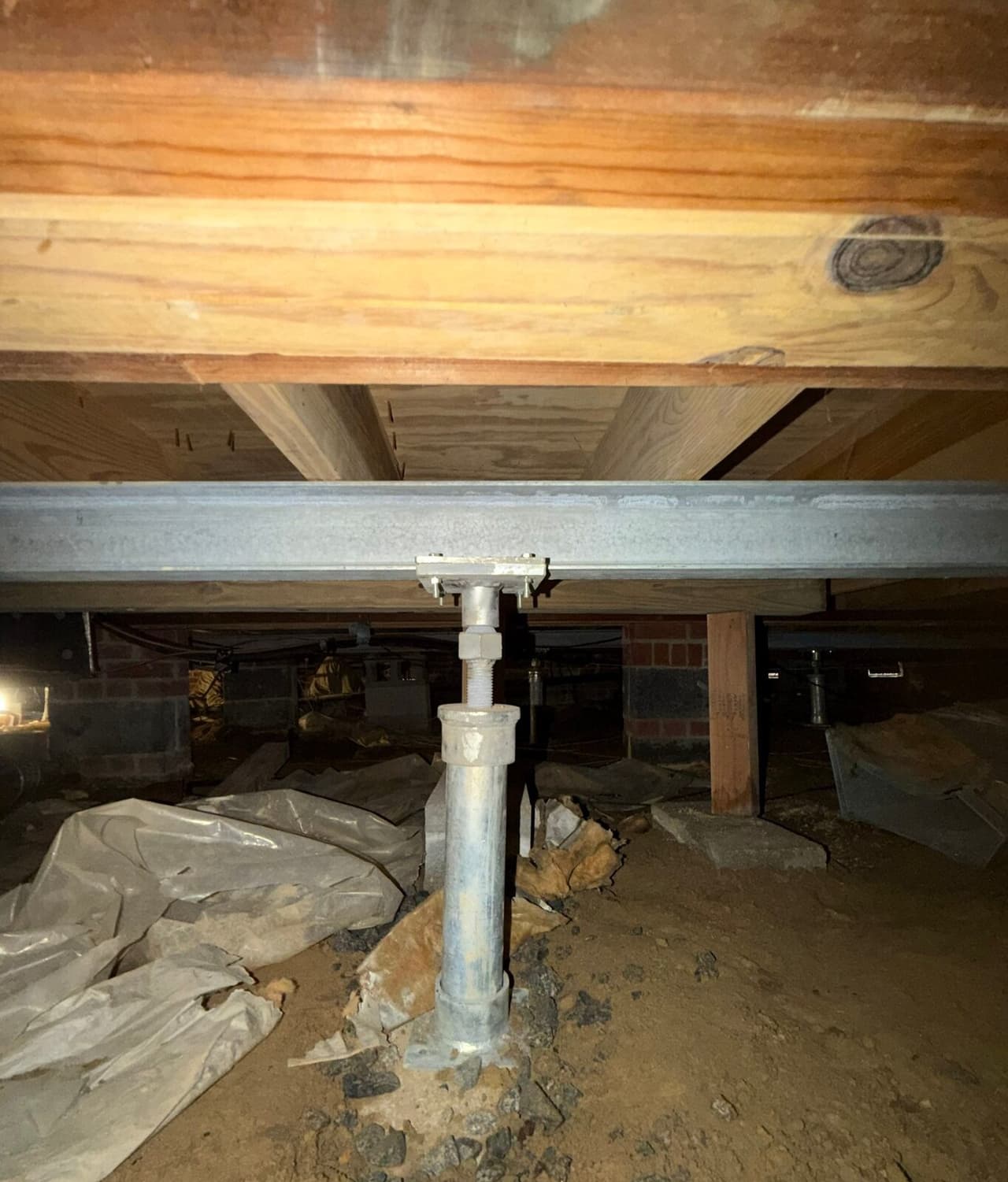Adjustable steel post on a gravel footing supporting a steel beam under a wood girder in a crawl space.