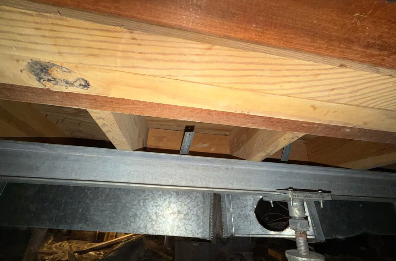 Steel beam under a wood girder with an adjustable post head bolted beside metal ductwork.