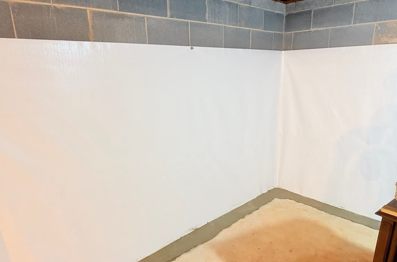 Basement corner with white wall membrane and a patched concrete perimeter strip along the floor.