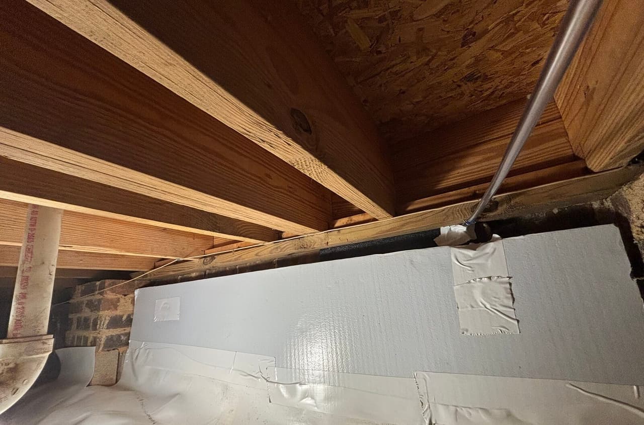 Foam board insulation on a crawl space wall with taped seams meeting a white floor liner.