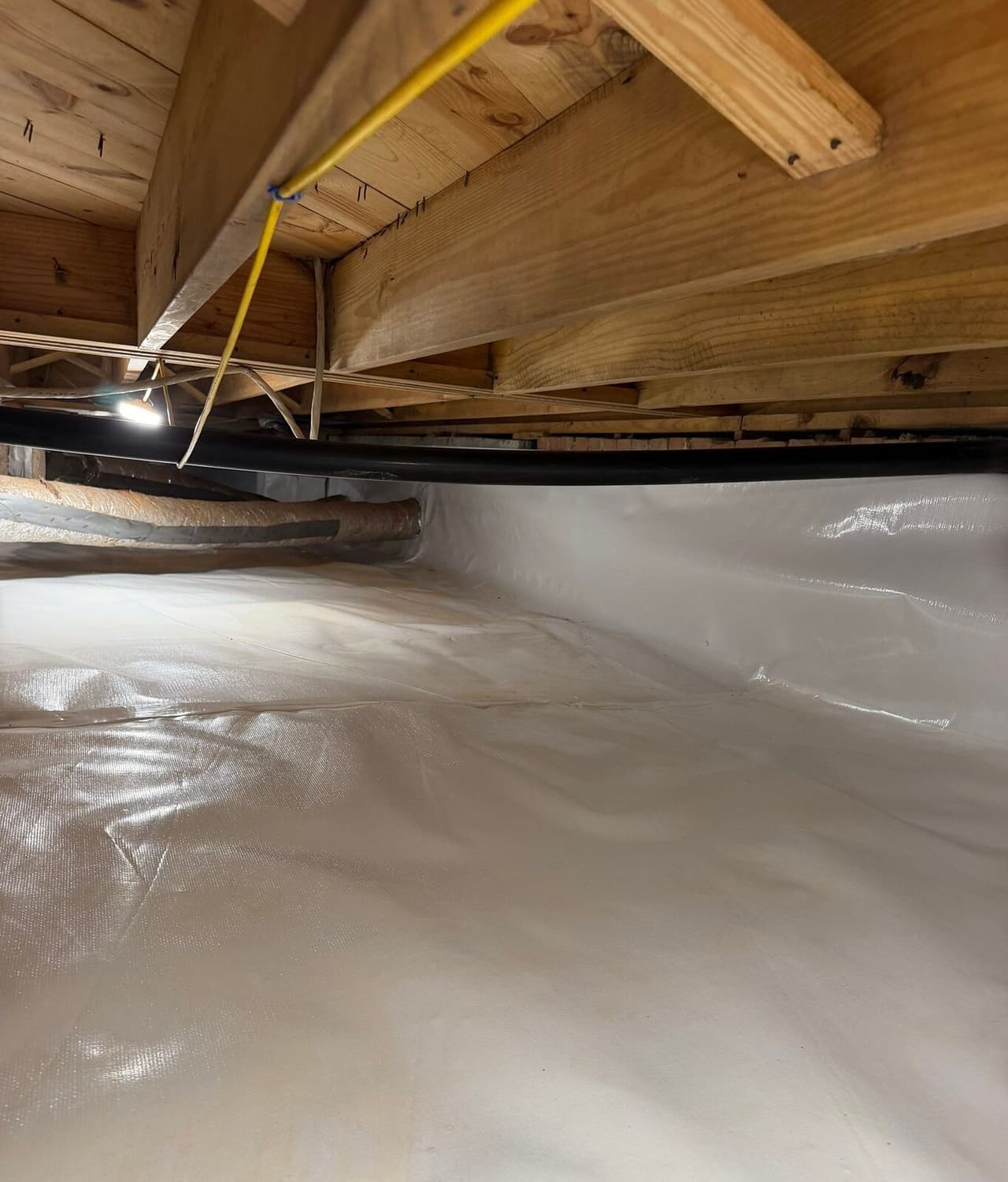 White liner covers the crawl space floor and runs up the wall below wood joists.
