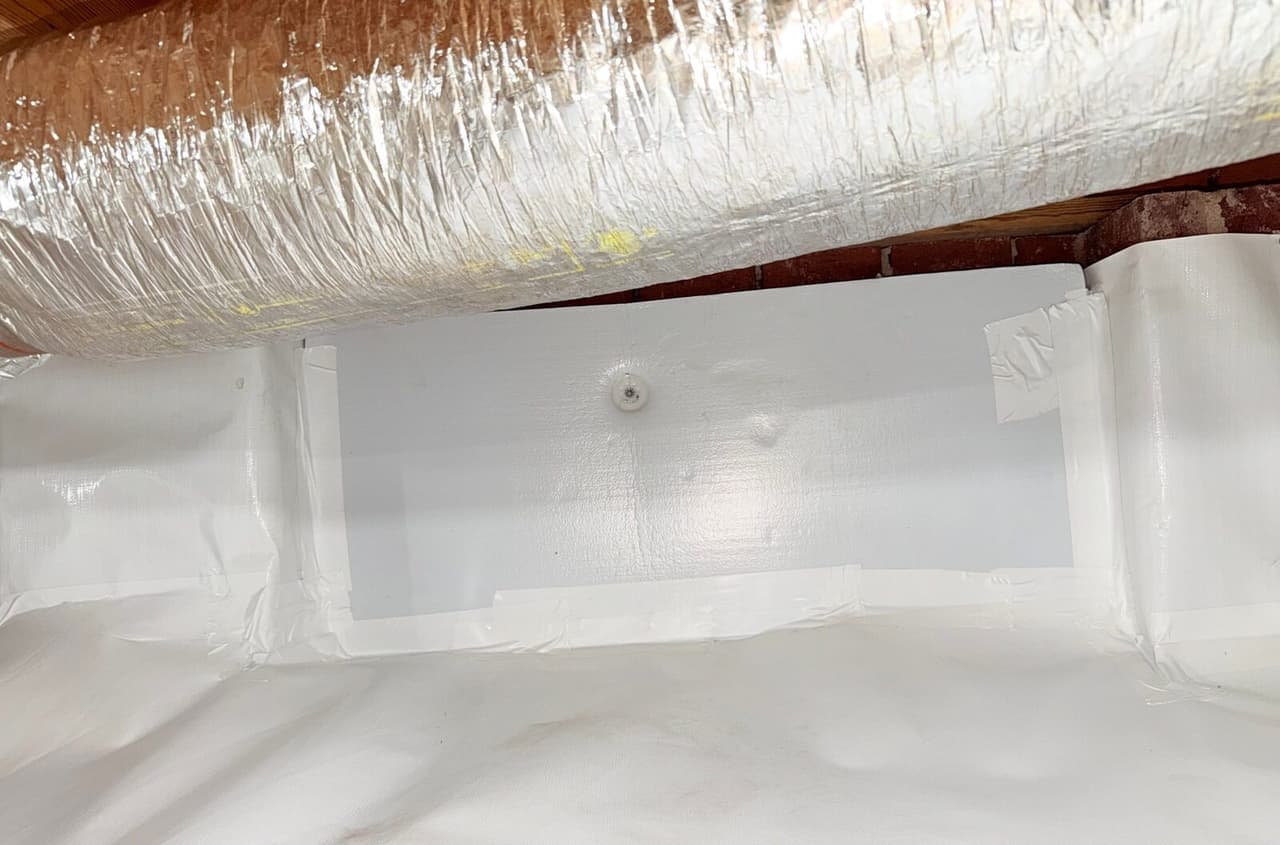 Close view of white wall liner with a fastener and taped seams beneath a silver duct.