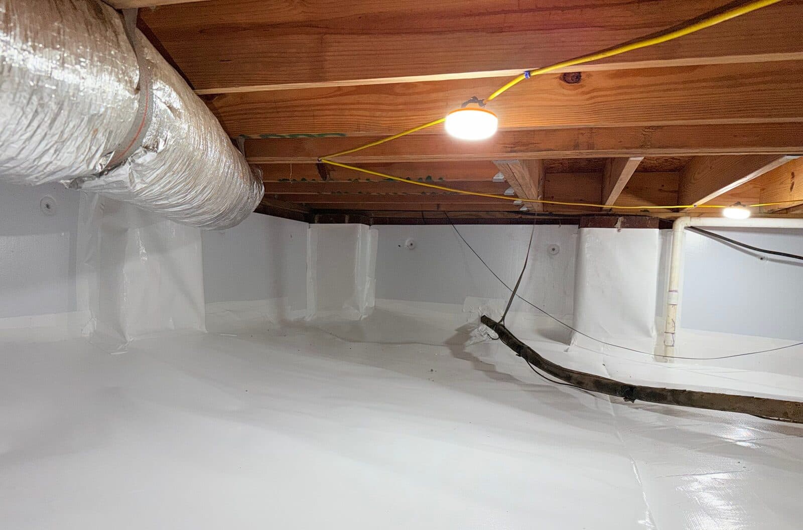 Wide view of crawl space with white liner covering floor, walls and piers under work lights.