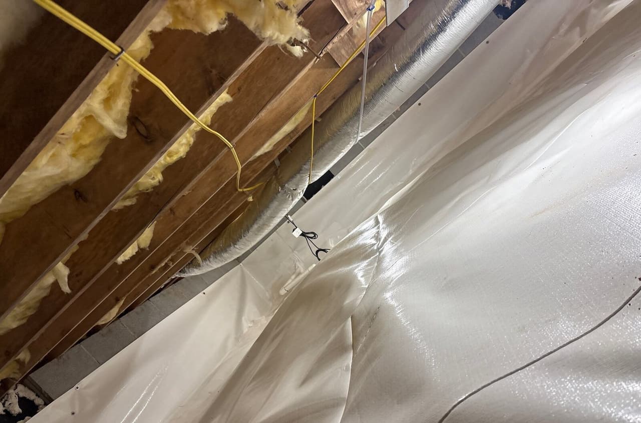 White liner fastened to crawl space walls and covering the floor beneath wooden joists.