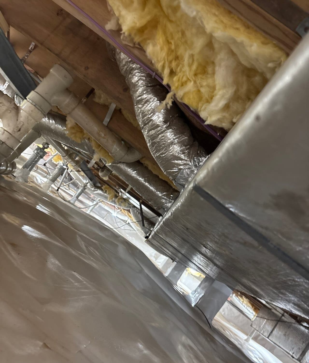 White liner covering a crawl space floor under ductwork, pipes and support posts.