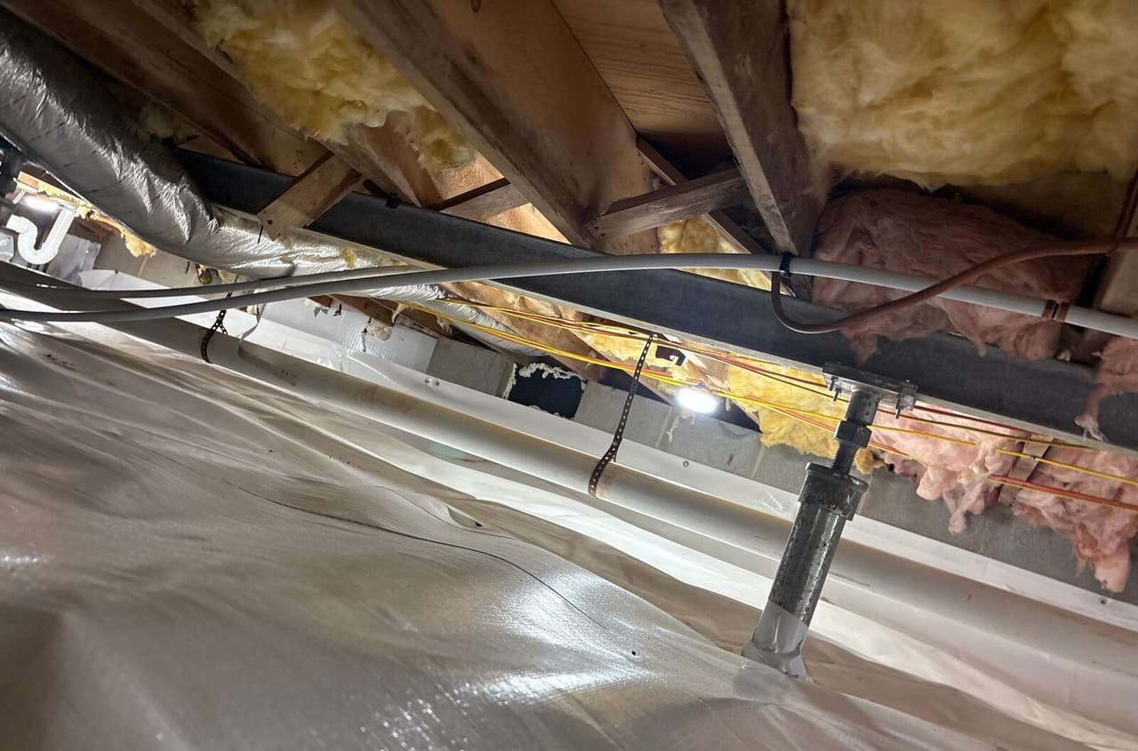 Steel support post under a beam, with white liner covering the crawl space floor below pipes and wiring.