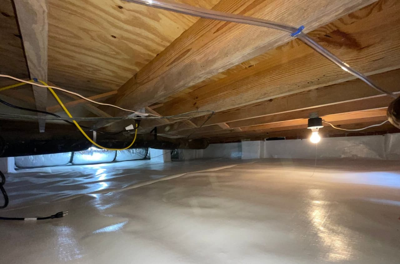 Crawl space with white liner on the floor and walls, wiring along the joists and a cord on the floor.