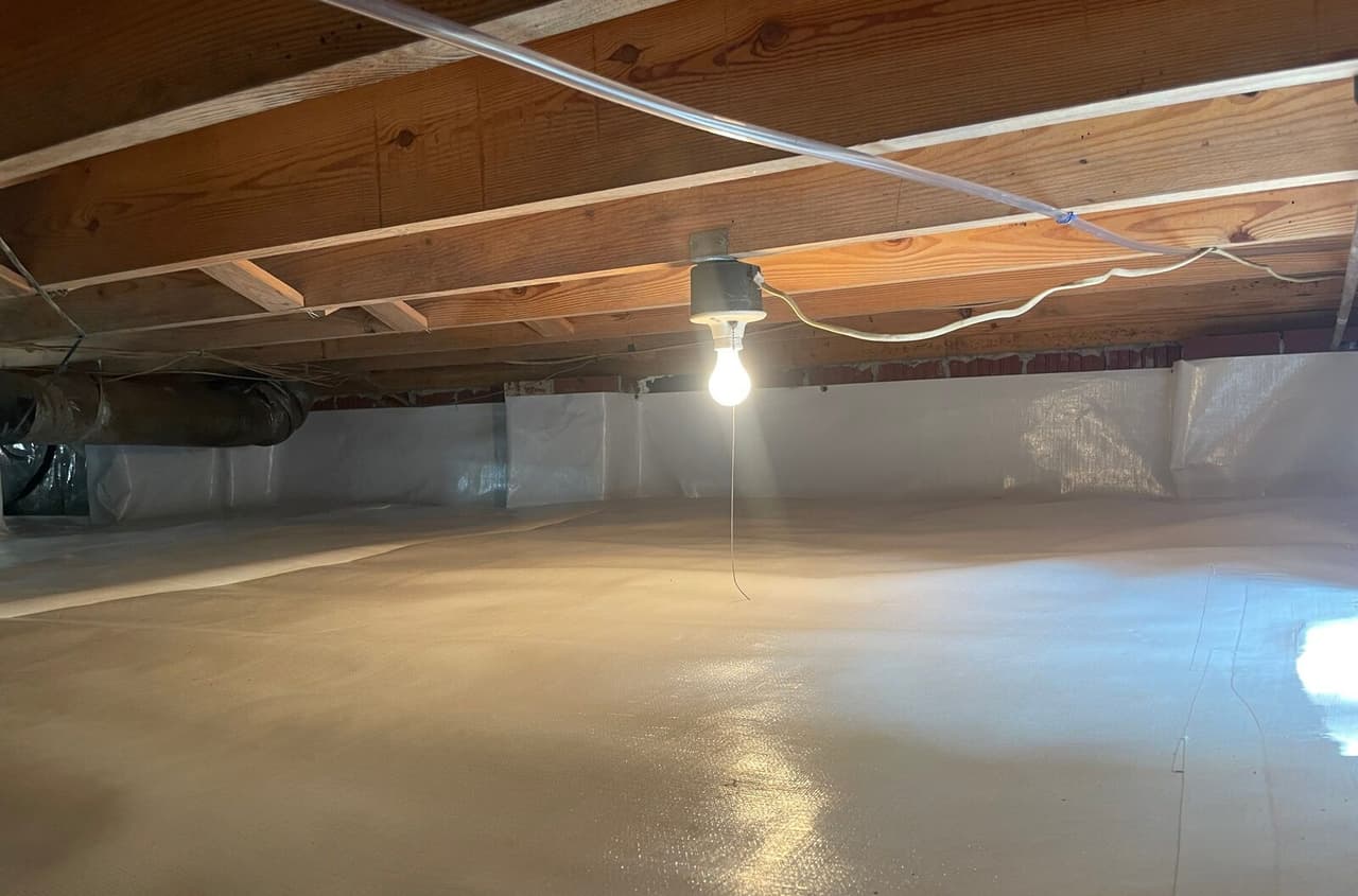 Lined crawl space floor and walls lit by a single bulb hanging from the joists.