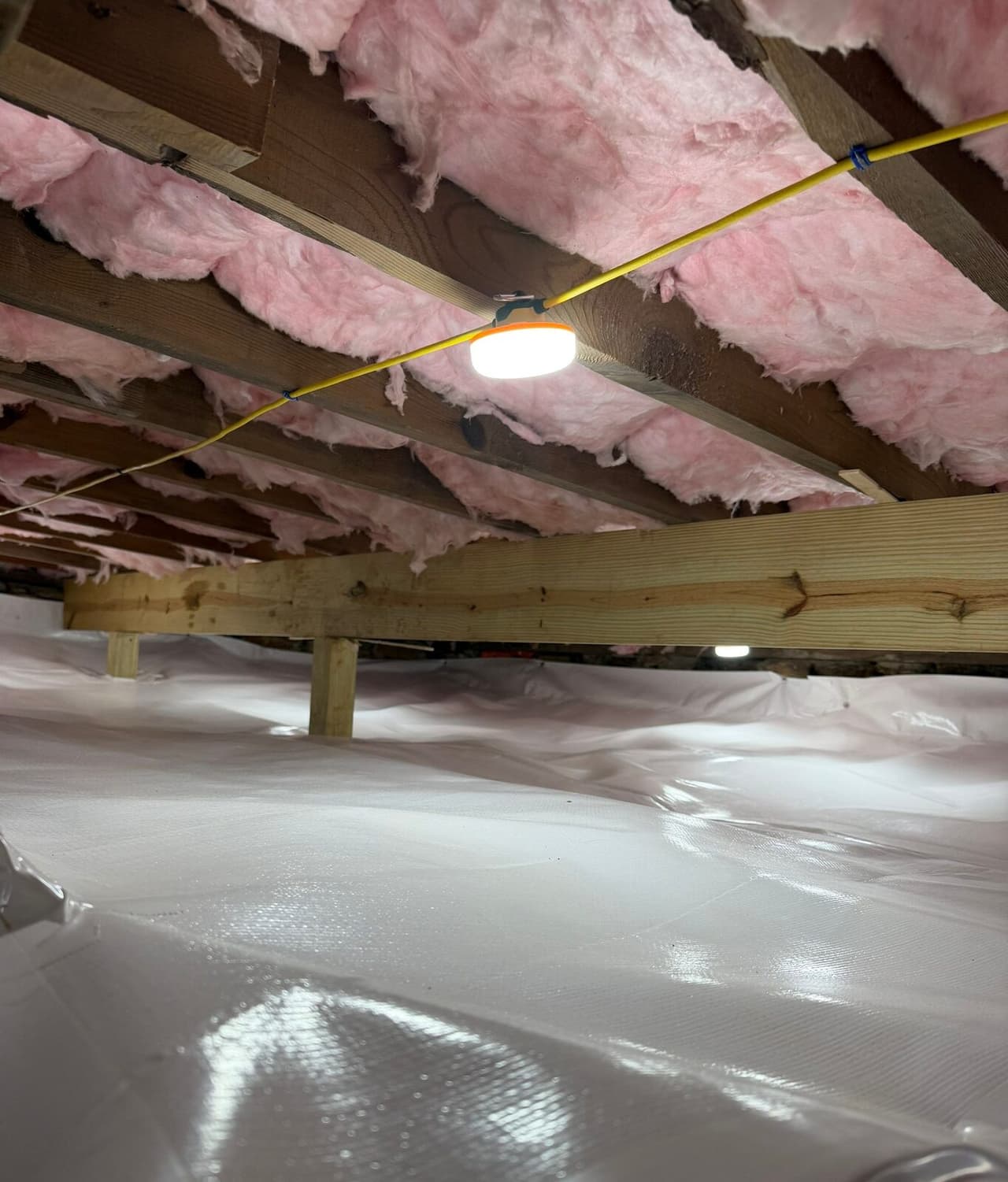 New wood beam on posts above a white lined crawl space floor with a work light on the joists.