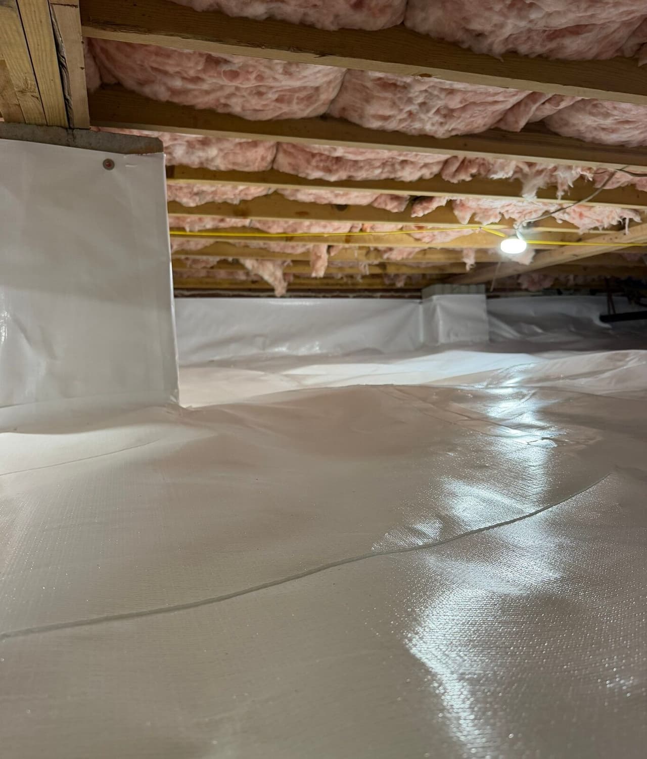 Wide view of a crawl space floor and walls covered in white liner with a sealed seam.