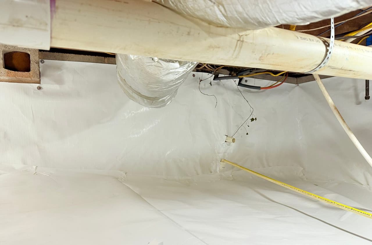 White liner covering crawl space walls and floor below a large pipe and a foil duct.