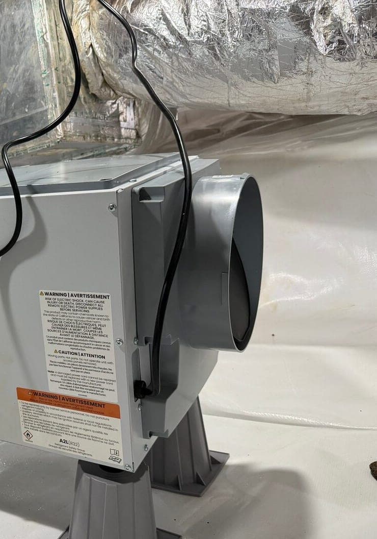 Branded dehumidifier on gray stands over white liner with drain line and condensate pump.