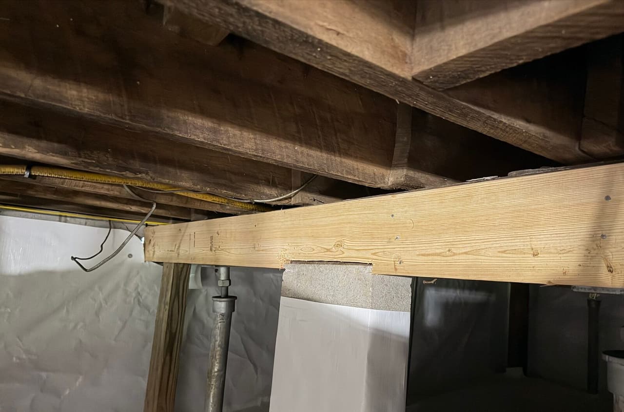 New lumber beam resting on a wrapped masonry pier with white liner on the crawl space walls.