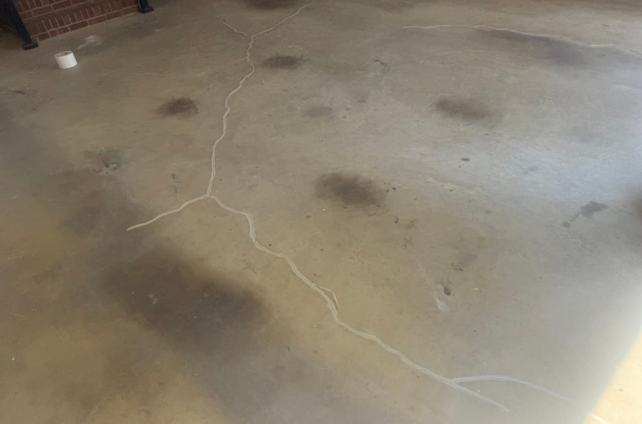 Wide view of a stained concrete floor with branching cracks sealed in white filler.