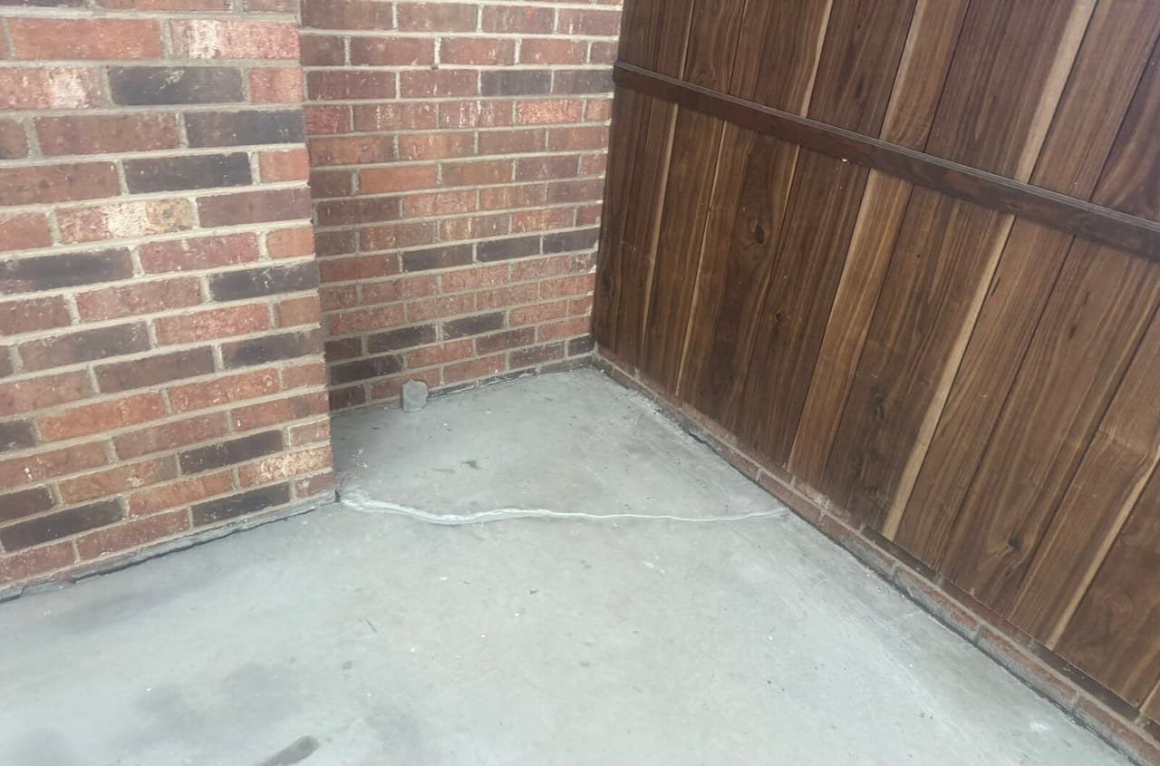 Floor crack sealed with white filler in a corner between a brick wall and wood paneling.