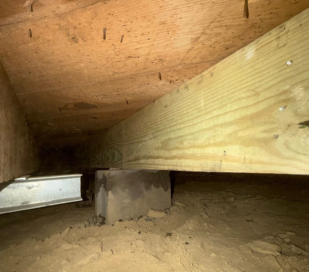 New treated wood beam on a block pier under the subfloor with a steel beam end nearby.