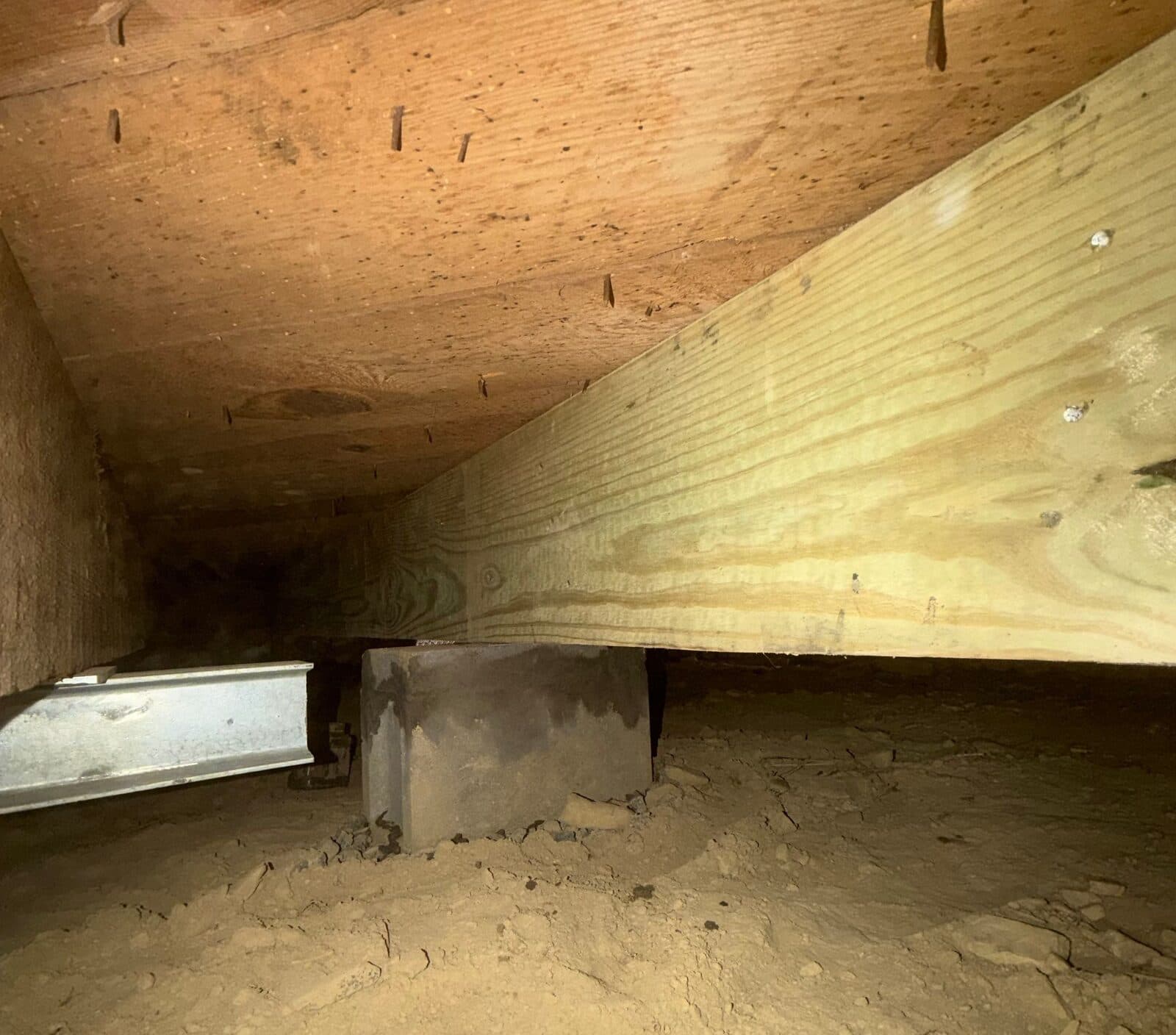 New treated wood beam on a block pier under the subfloor with a steel beam end nearby.