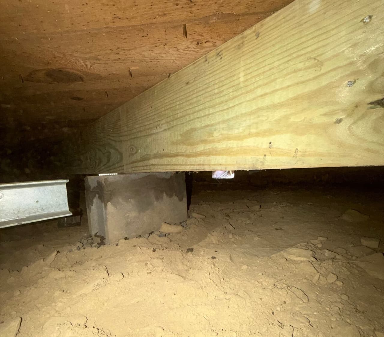 New treated wood beam resting on a concrete block pier beside a steel beam in a crawl space.