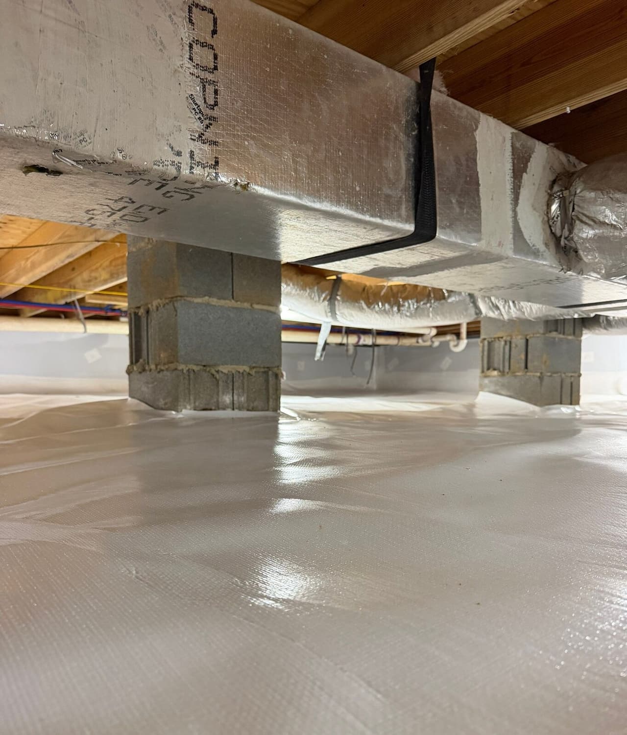Block piers and a duct trunk above a crawl space floor covered with white liner.