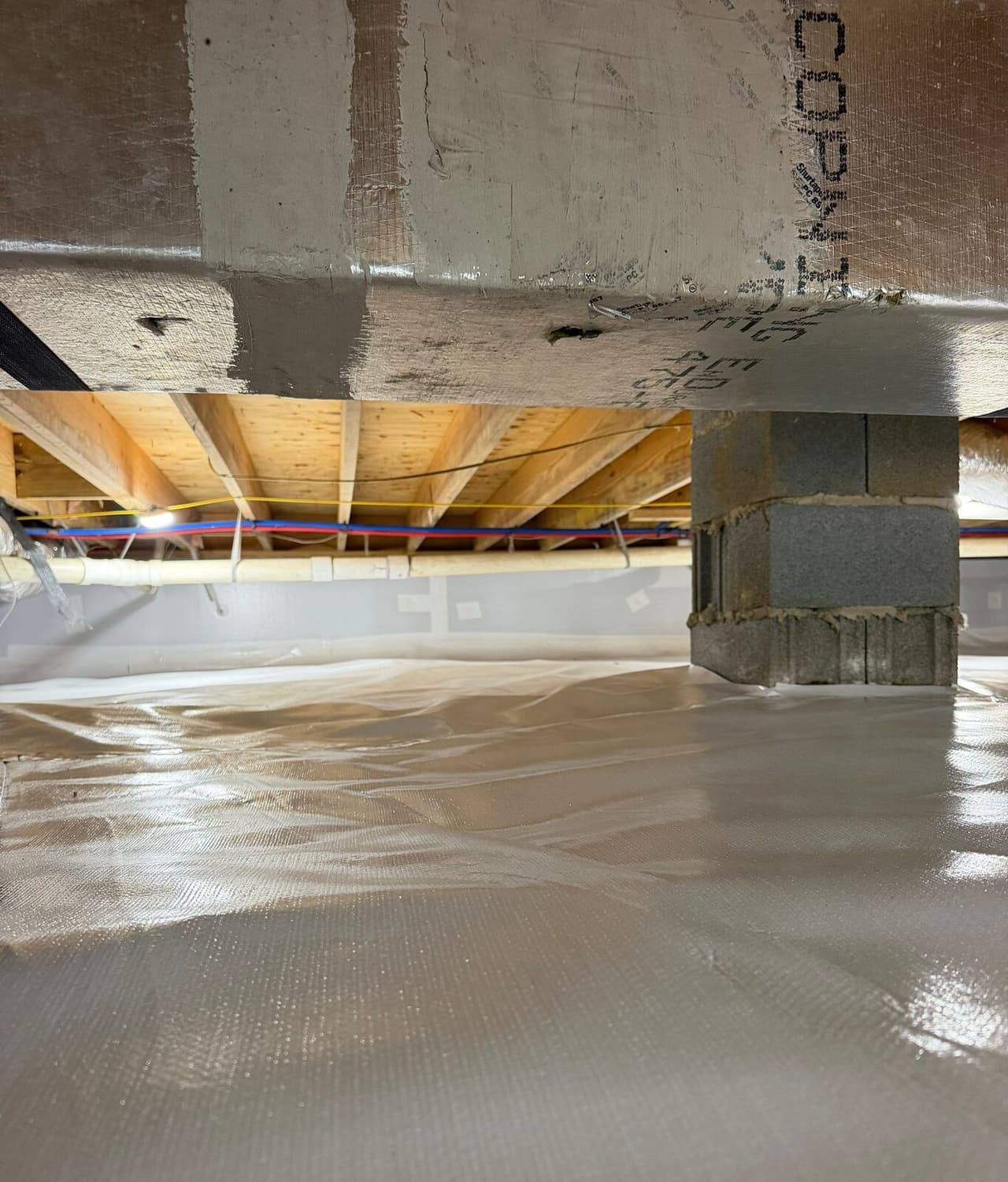 Duct trunk and block pier over a white lined crawl space floor.