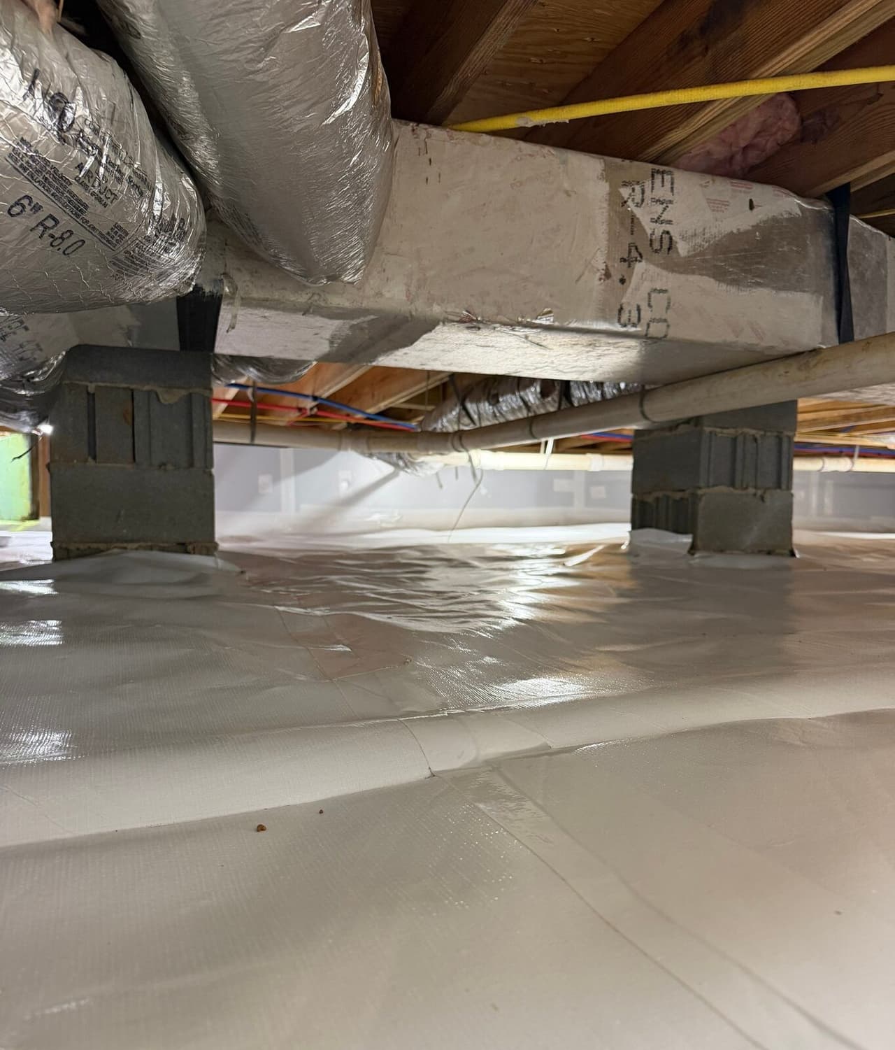Block piers and ducts above a crawl space floor with taped white liner seams.