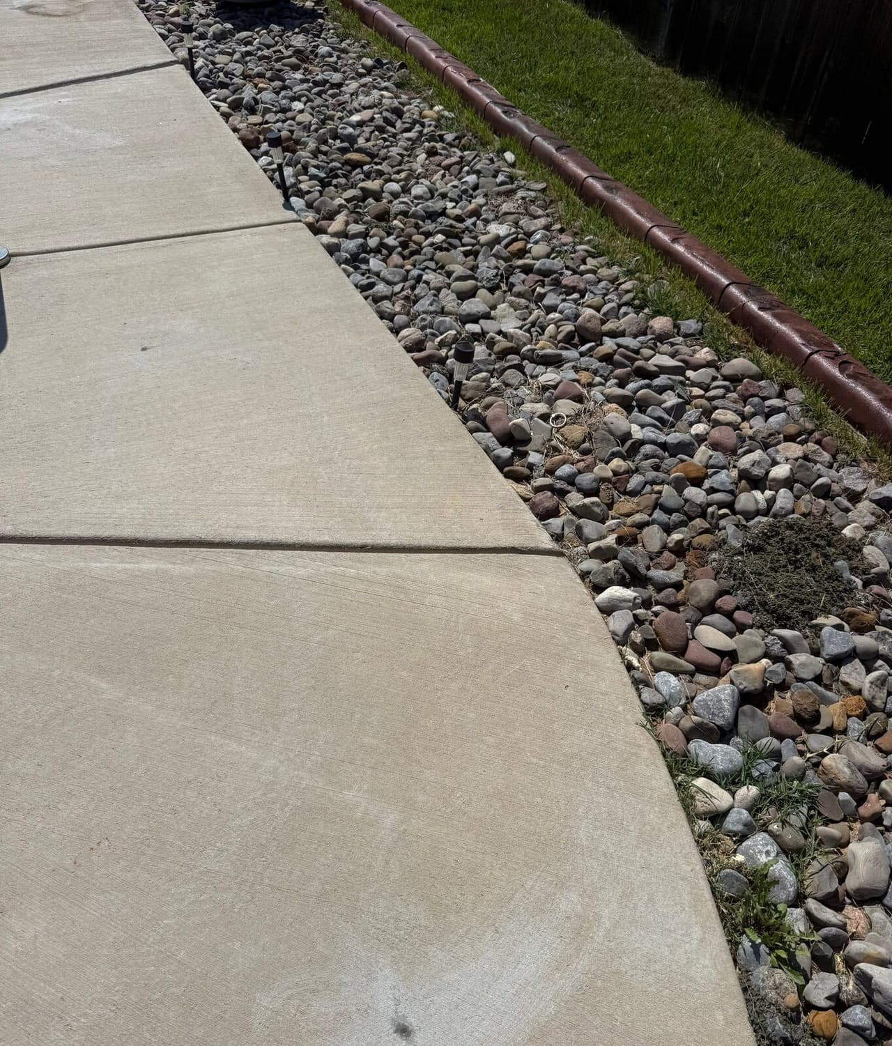 Concrete pool deck slabs sitting flush along a river rock border with a patched injection hole near the bottom.