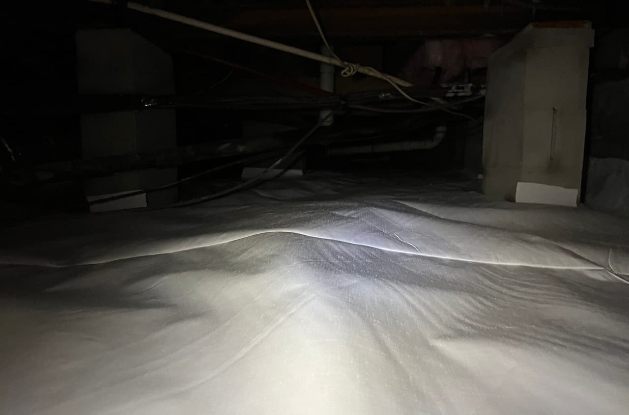Crawl space liner over the floor beside a block pier.