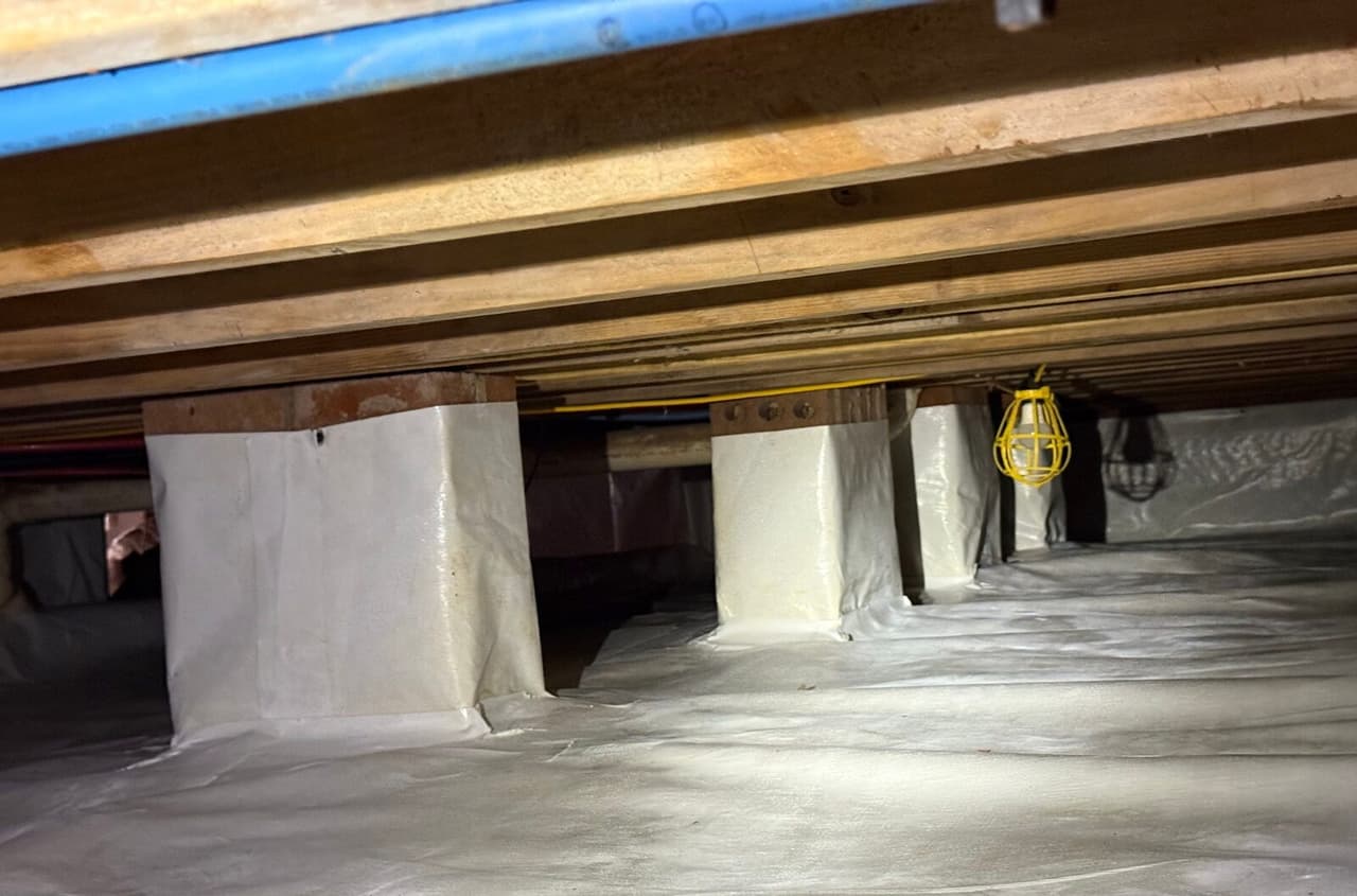 Row of piers wrapped in white liner over a lined crawl space floor with a work light.