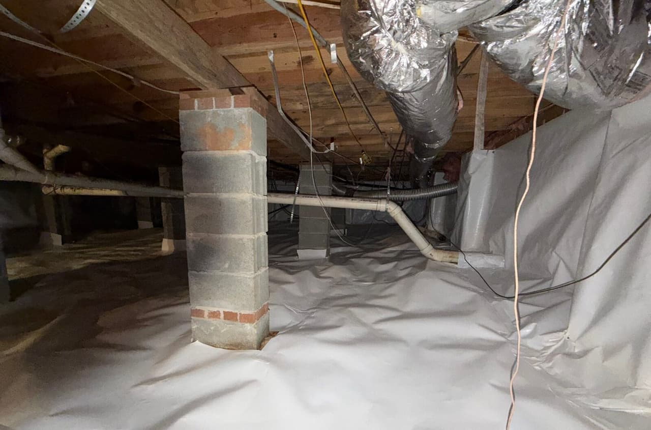 Crawl space with white liner on floor and walls around block piers and ductwork.