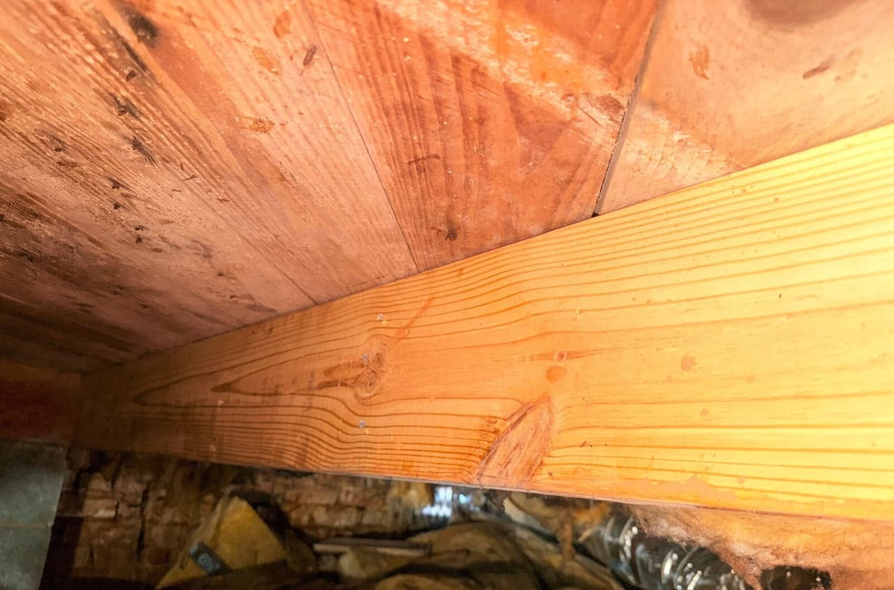 New wood joist fastened beneath an older subfloor with a brick foundation wall below.