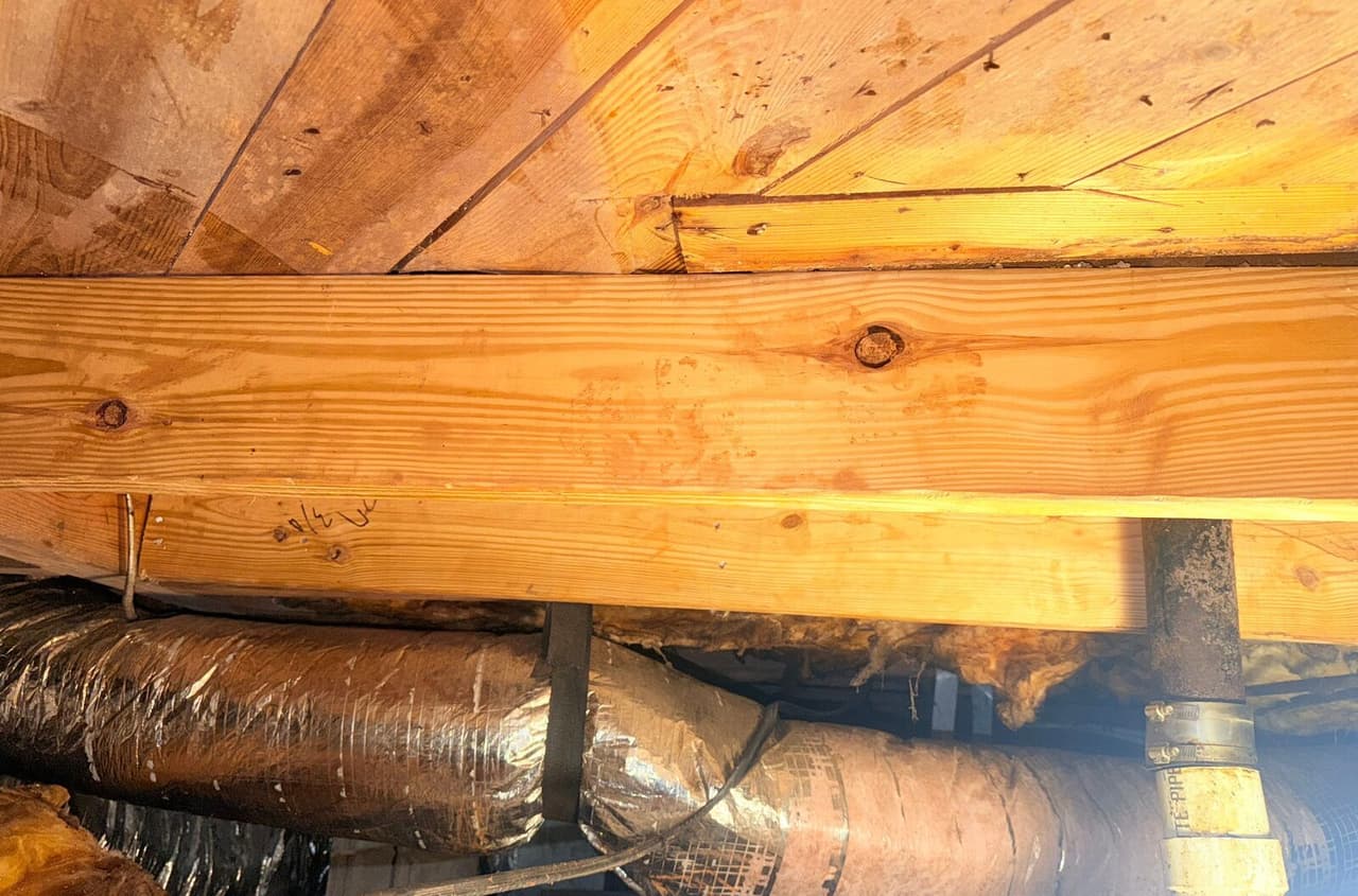 New sistered lumber fastened under a subfloor above foil ductwork and a drain pipe.