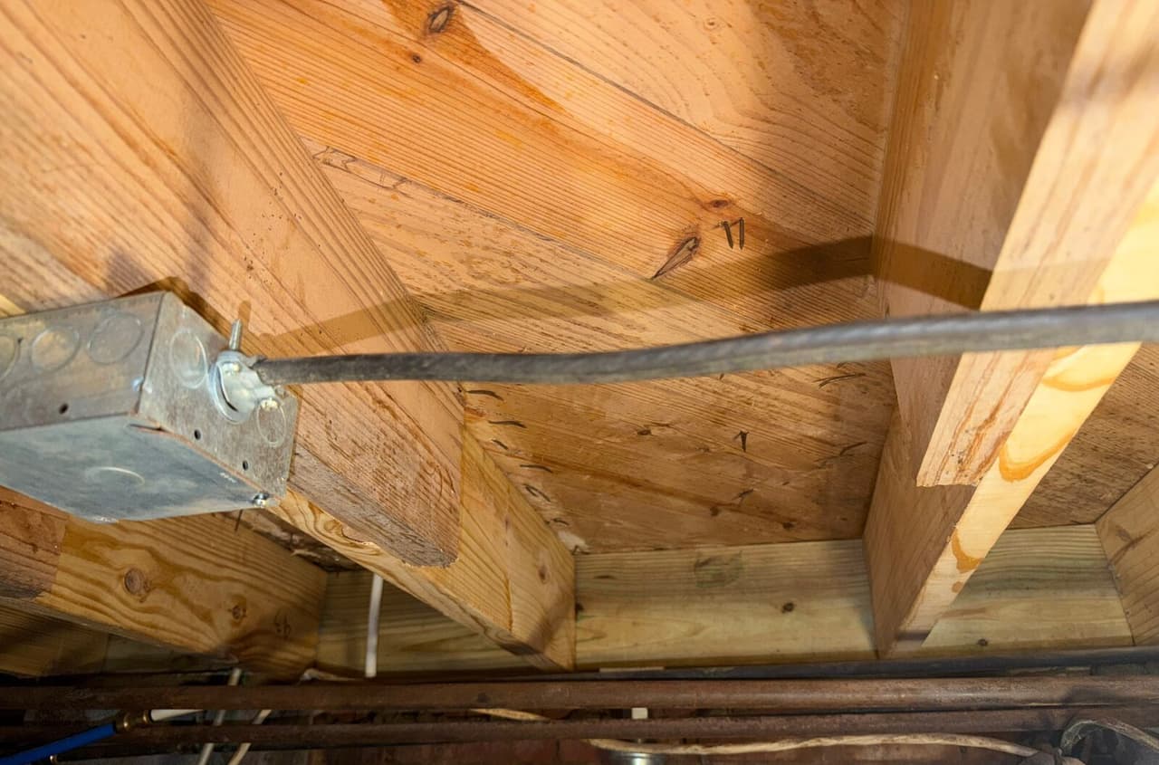New wood blocking and sistered joists nailed in place under a subfloor beside a metal electrical box.