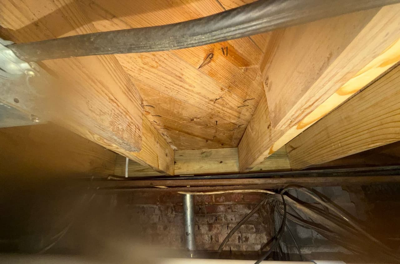 New lumber joists and blocking fastened under a crawl space subfloor above a brick foundation wall.