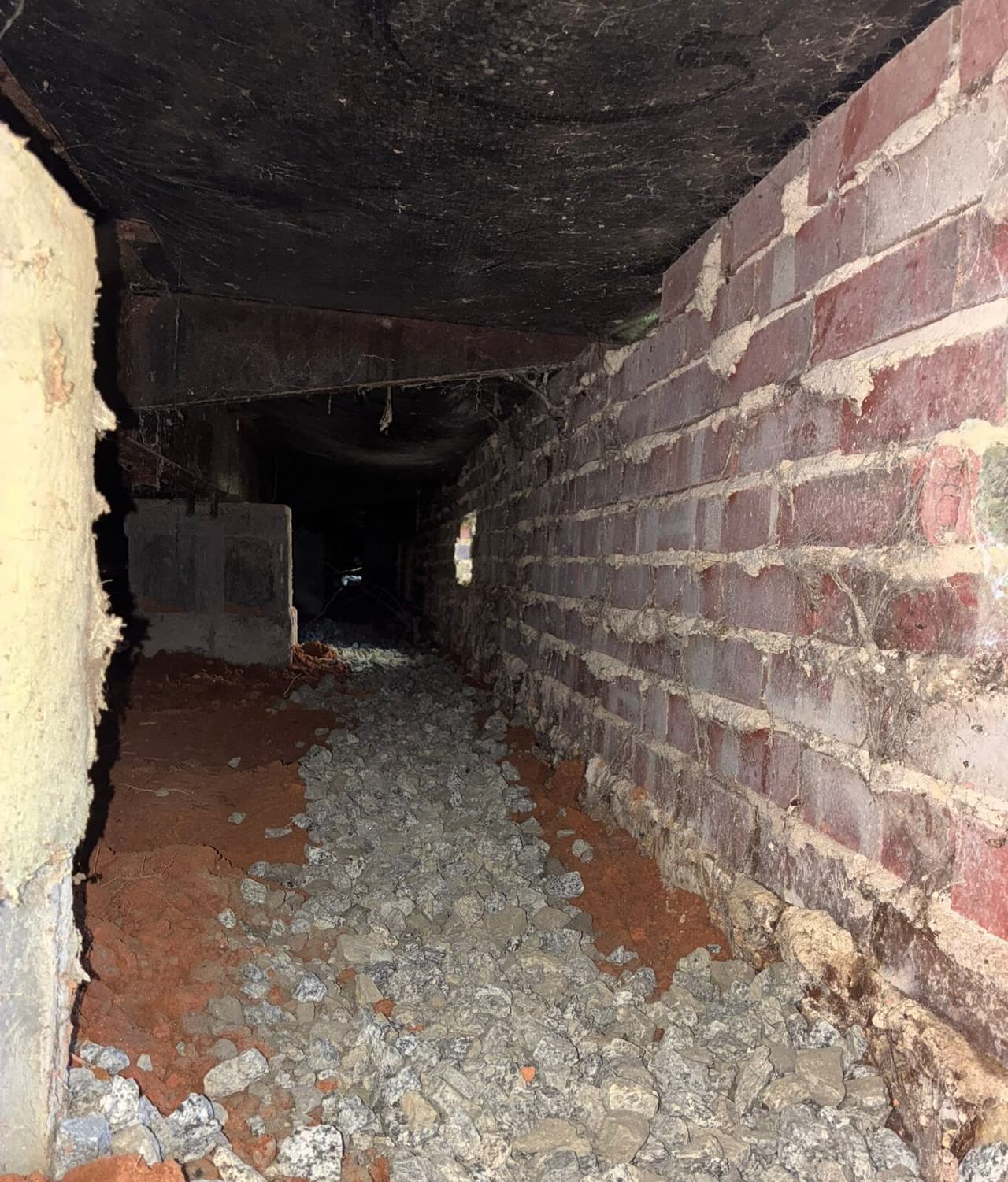 Long gravel filled drain trench running along a brick crawl space wall.