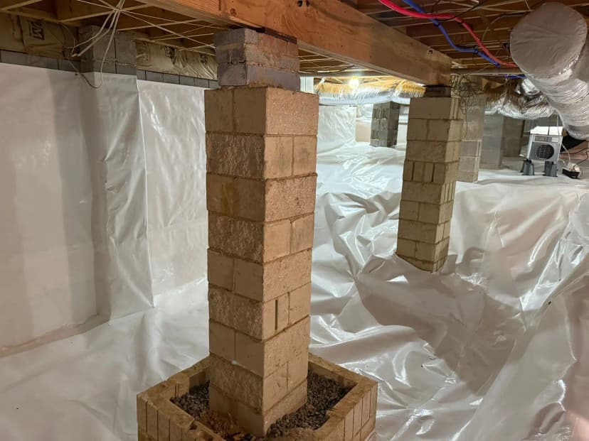 Block piers standing on a white vapor barrier in a crawl space